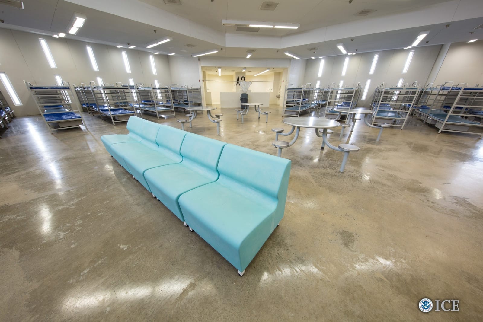 An empty dormitory at the Port Isabel Detention Center: rows of bunk beds, steel tables and a long bench.