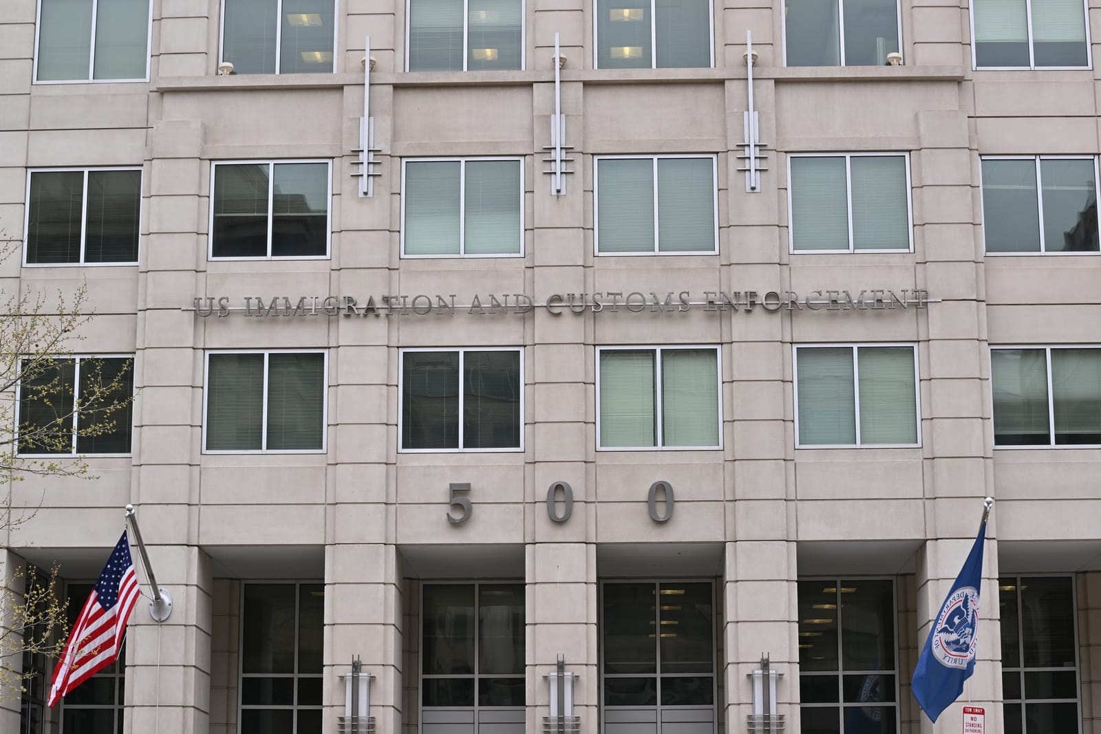 Front of the Immigration and Customs Enforcement headquarters building, 500 12th Street SW, Washington, DC, with flags and agency name above the entrance.